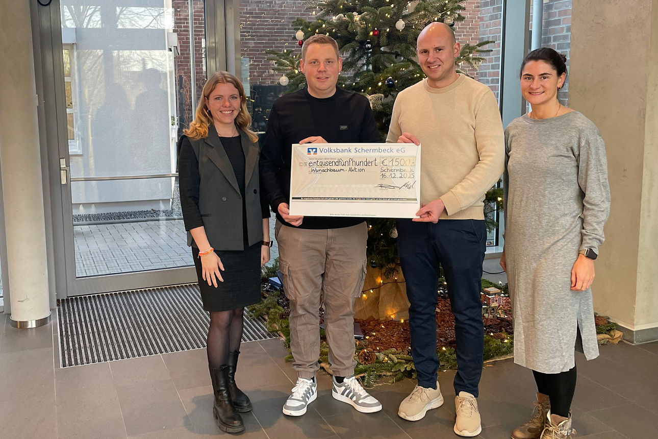 Zwei Frauen und zwei Männer vor einem geschmückten Weihnachtsbaum mit einem Spendenscheck.