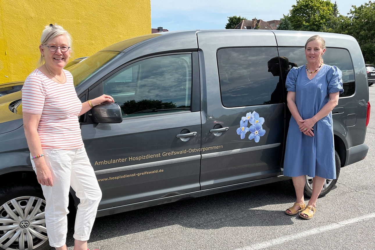 Zwei Frauen vom Hospizdienst stehen vor dem Dienstfahrzeug