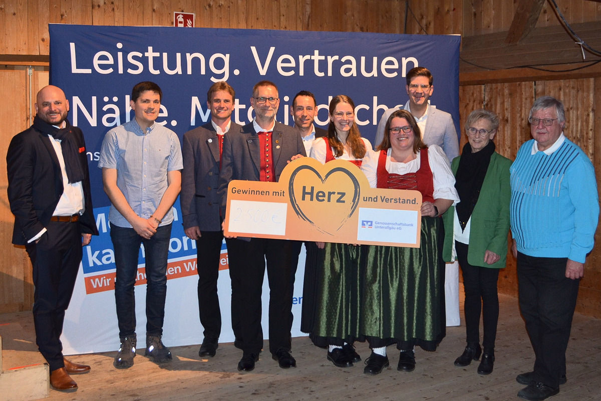 Mitgliedes des Musikvereins stehen mit großem Pappschild mit Herz nebeneinander vor einer Leinwand