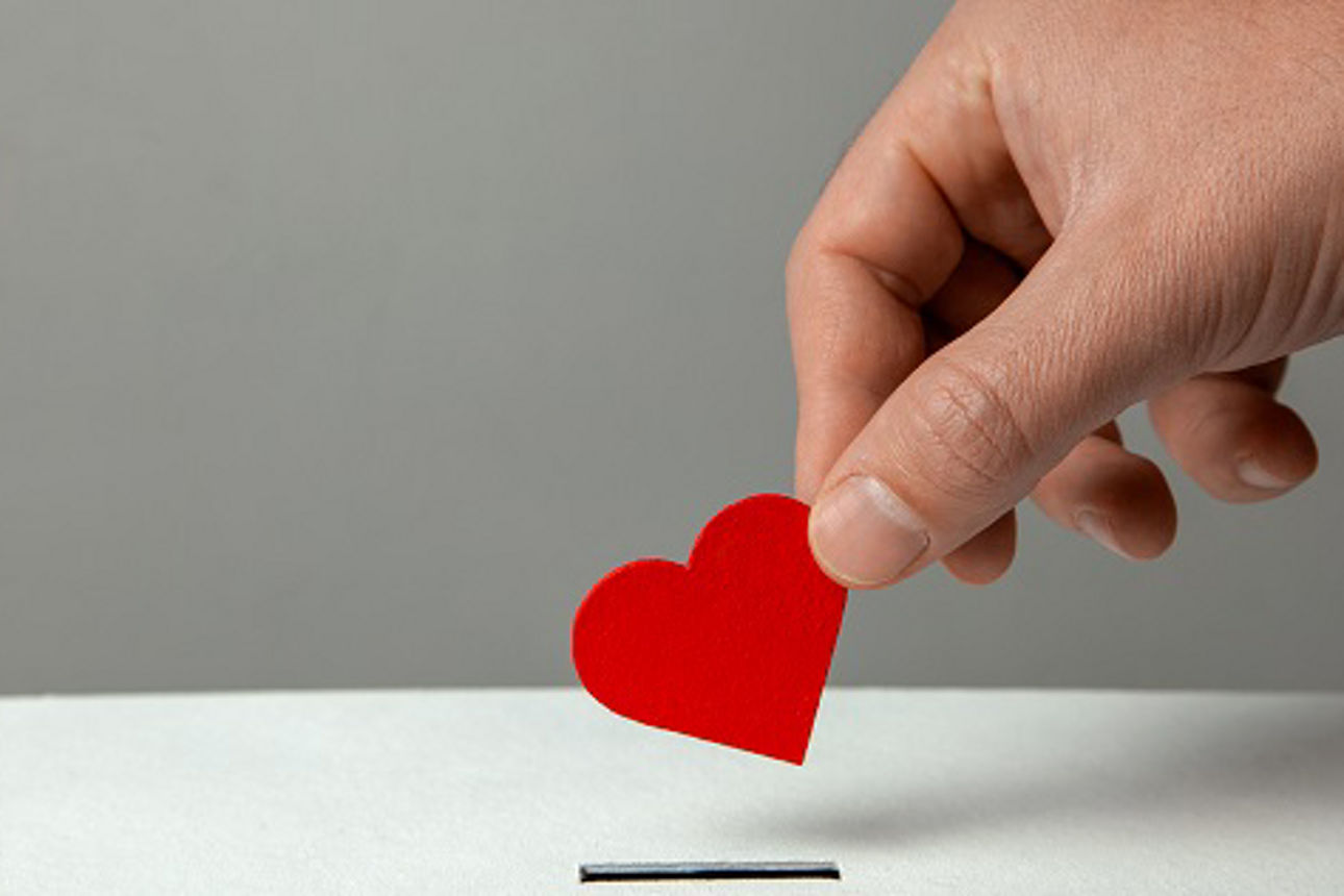 Man’s hand places heart in the donation slot. The concept of the donor of blood or human organs, saving lives. Copy space for text
