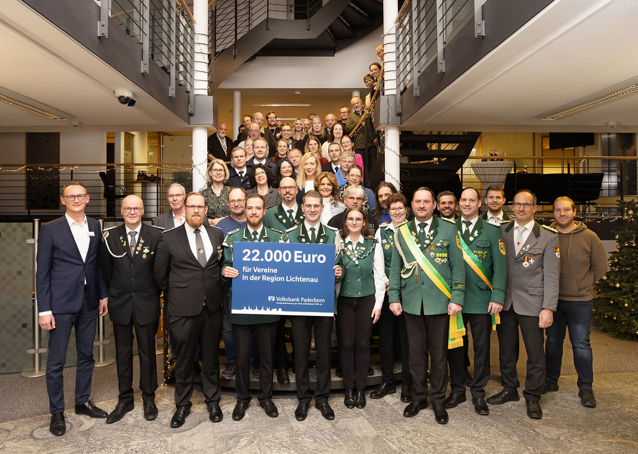 Eine Gruppe mit zahlreichen Vertreterinnen und Vertretern der Vereine in Lichtenau und dem Leiter des BeratungsCenters Lichtenau präsentieren einen Spendenscheck in den Räumlichkeiten der Bank auf einer Treppe
