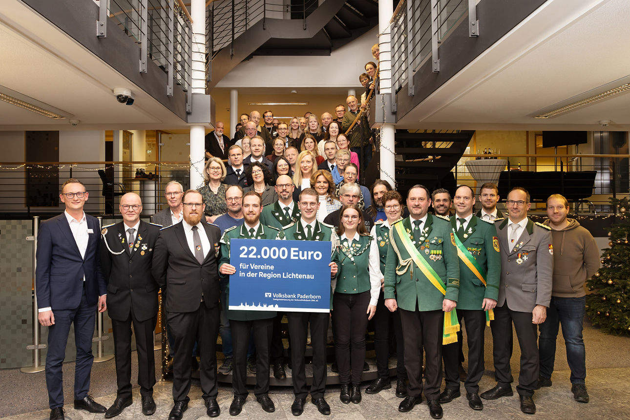 Eine Gruppe mit zahlreichen Vertreterinnen und Vertretern der Vereine in Lichtenau und dem Leiter des BeratungsCenters Lichtenau präsentieren einen Spendenscheck in den Räumlichkeiten der Bank auf einer Treppe