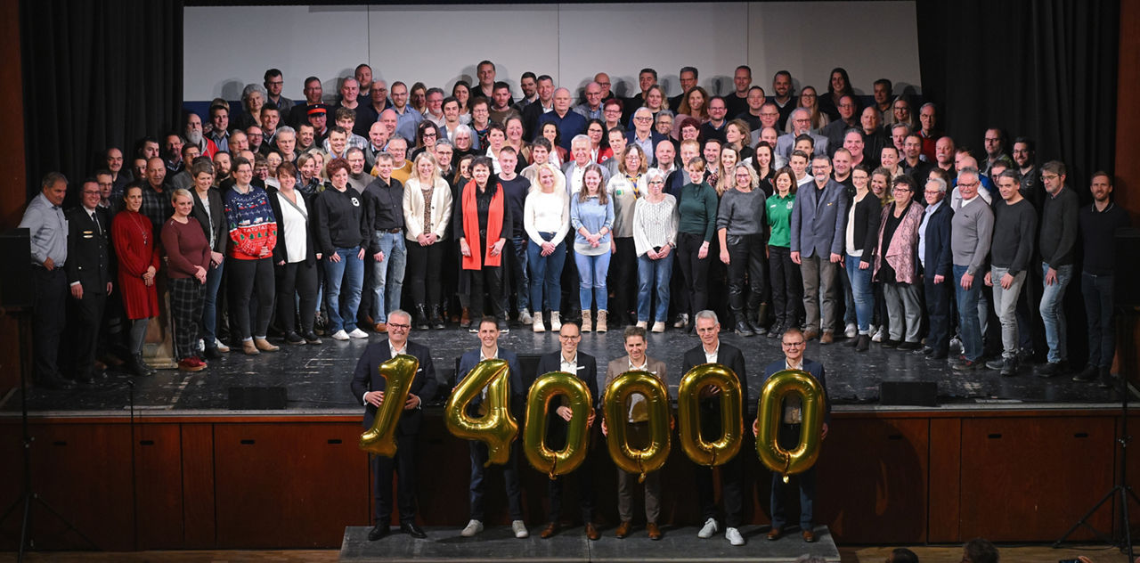 Gruppenfoto der Spendenempfänger im Vordergrund halten 6 Personen die Zahl 140.000