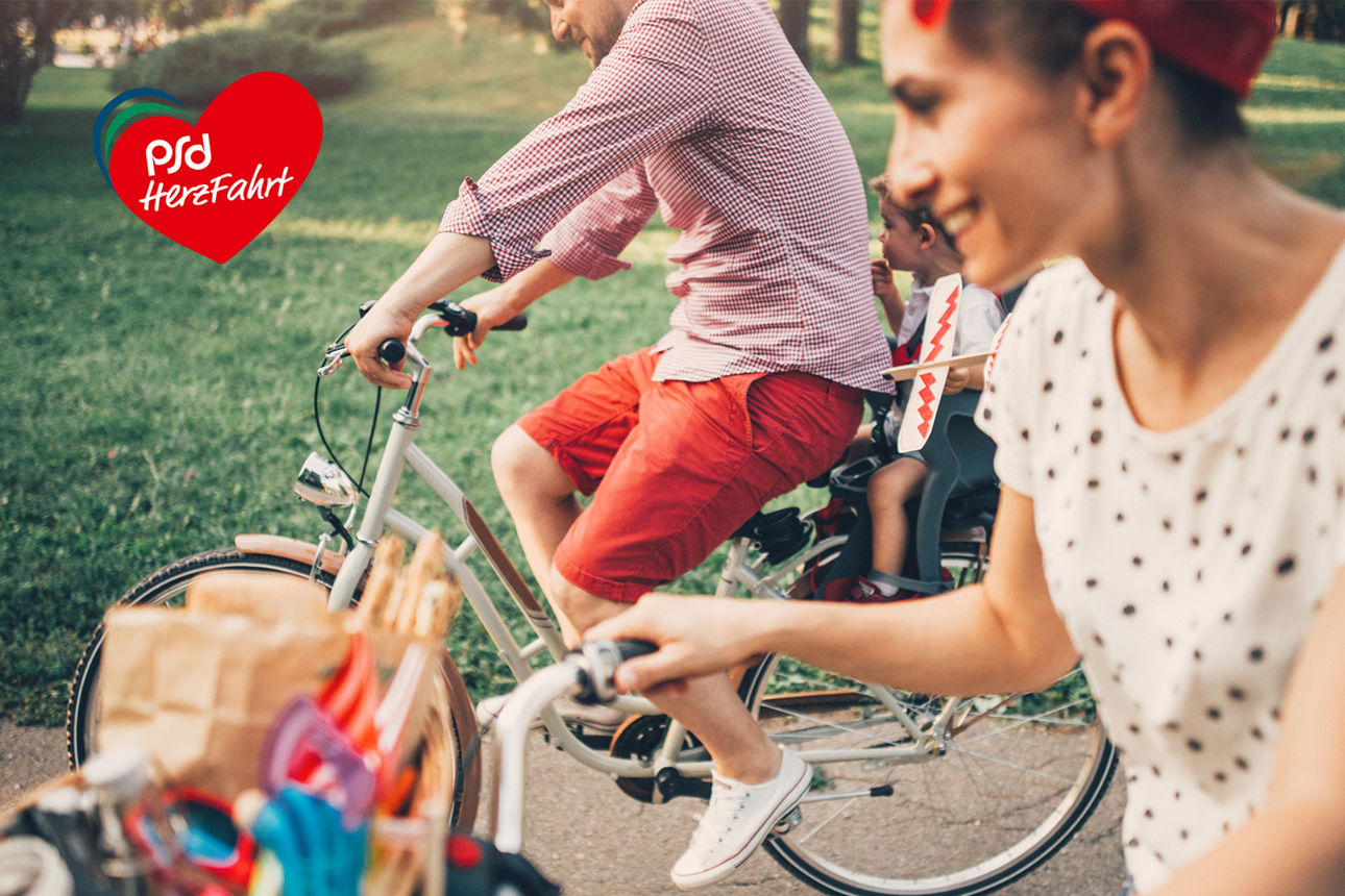 Eine junge Familie macht eine Fahrradtour und der kleine Sohn sitzt in einer Kinderschale auf dem Gepäckträger.