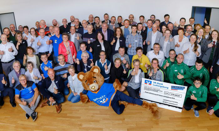 Viele Personen in einem Raum zum Gruppenfoto und einem riesigen Spendenscheck der VR-Bank Ludwigsburg