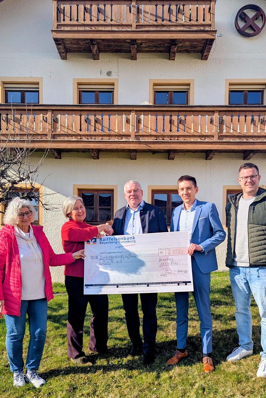 fünf Personen stehen vor einem Haus und halten einen symbolischen Scheck in den Händen