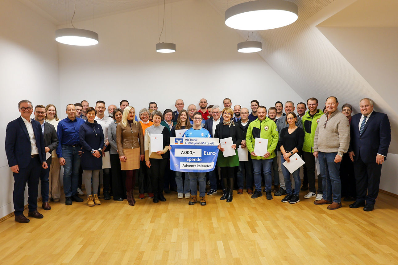 Einige Personen stehen in Reih und Glied und lächeln mit einem Spendenscheck in der Hand in die Kamera