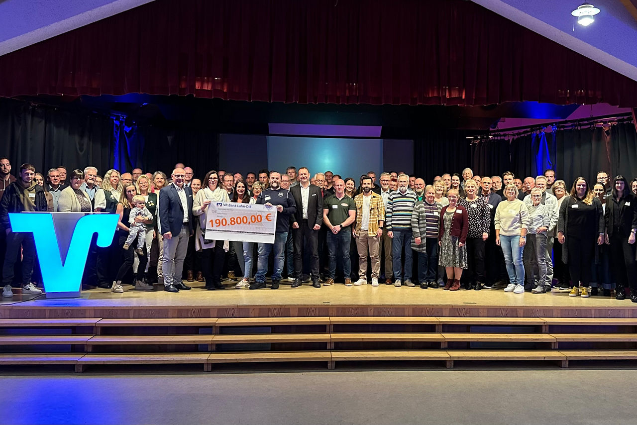 Gruppenfoto mit allen Gästen und Scheck auf der Bühne.