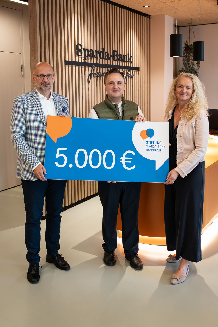 Drei Personen halten einen Spendenscheck im Wert von 5.000 Euro in den Händen