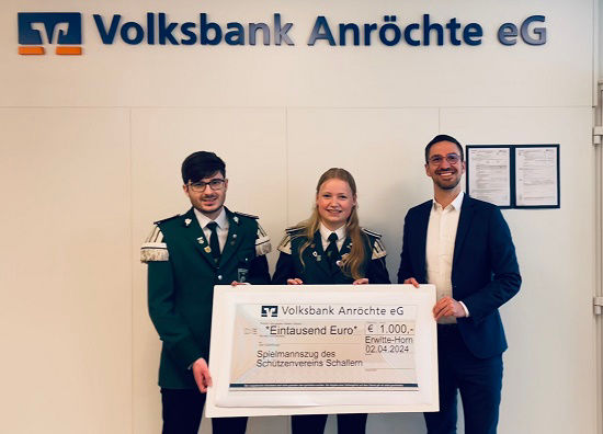 Zwei Beamte und ein Bankvertreter halten gemeinsam einen großen Scheck