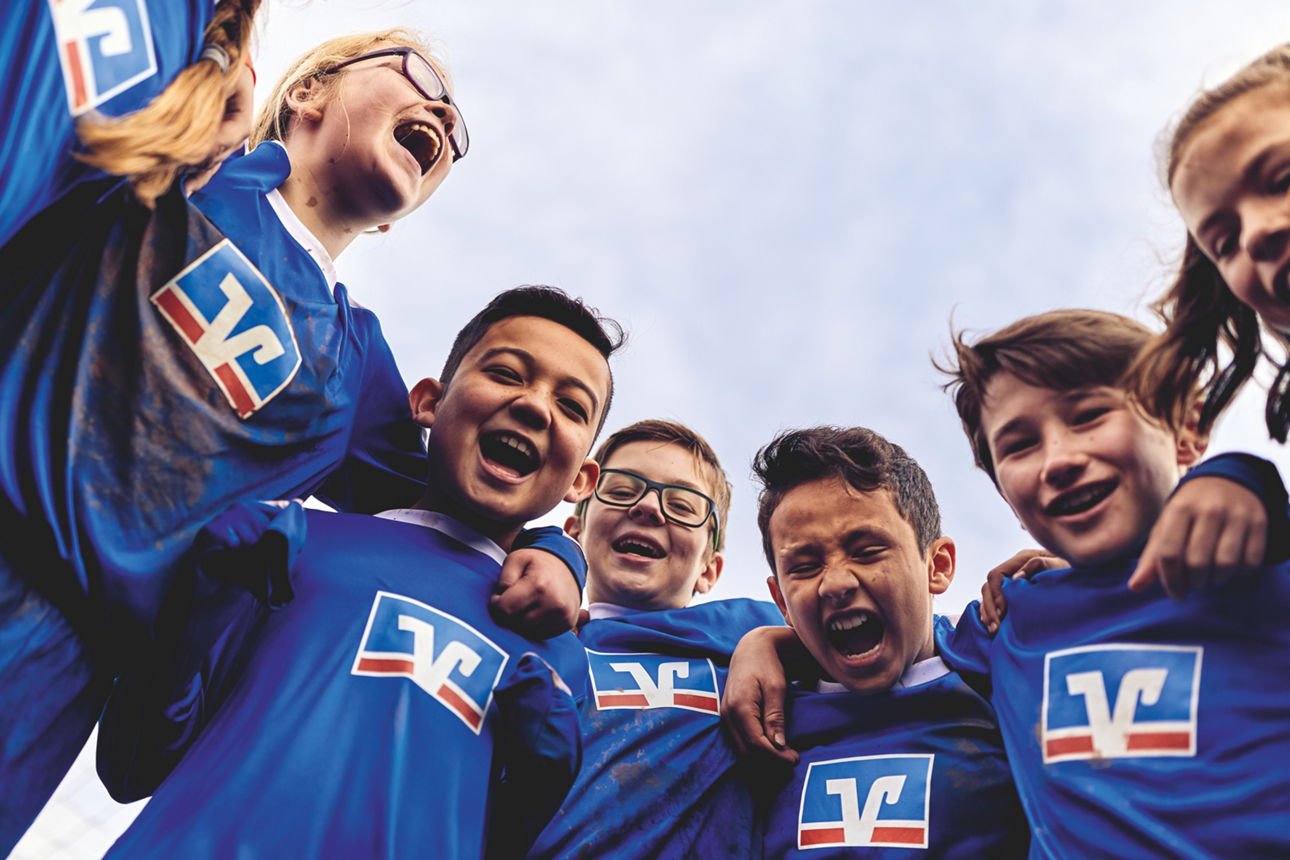 Kinder einer Fußballmannschaft in Volksbank-Trikots freuen sich über ihren Erfolg