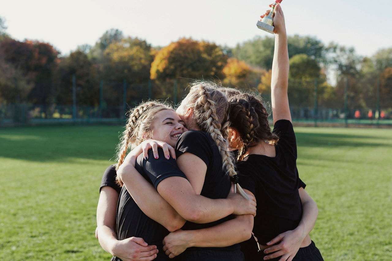Eine Gruppe junger Frauen strecken auf einem Sportplatz einen Pokal in die Luft