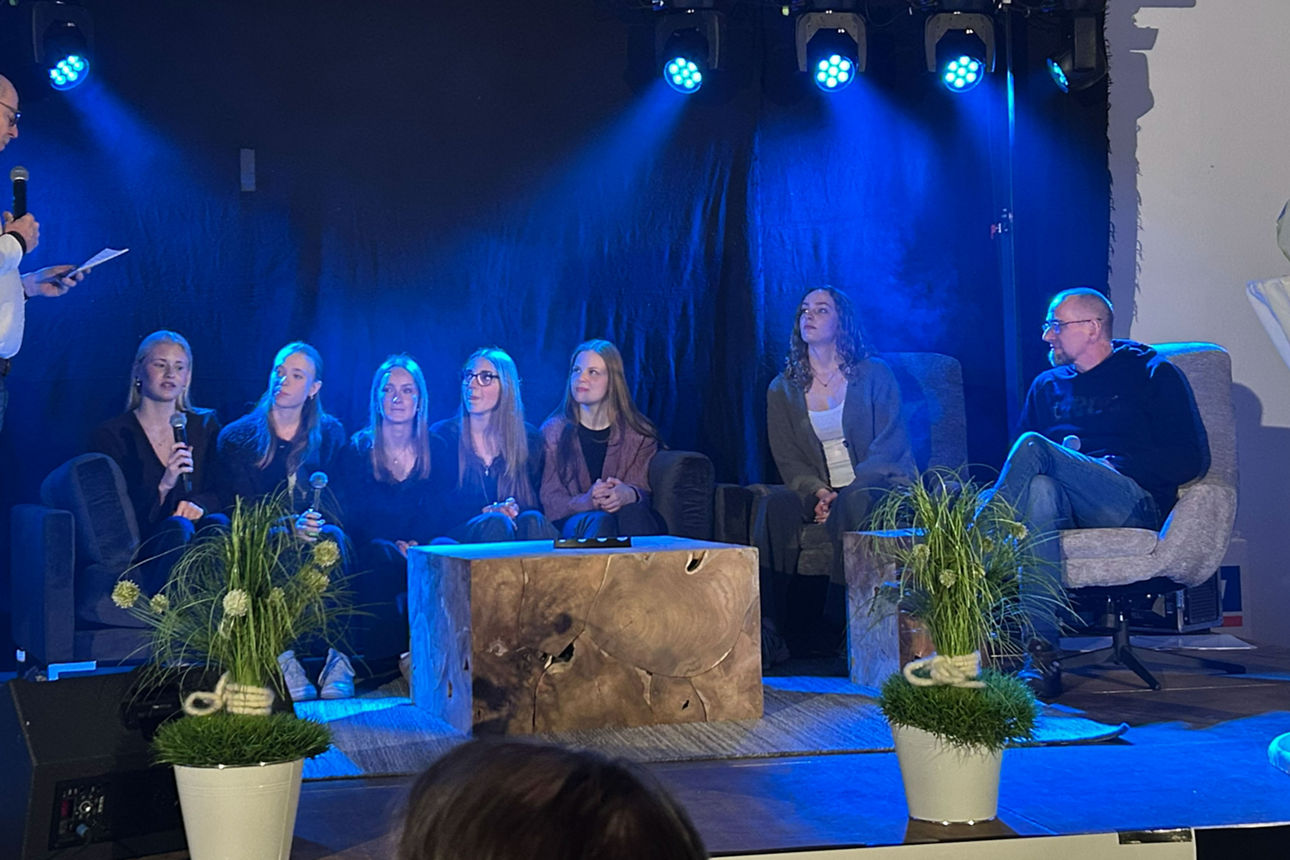 Sieben Personen sitzen auf einer Couch bzw. auf Sesseln und werden interviewt.