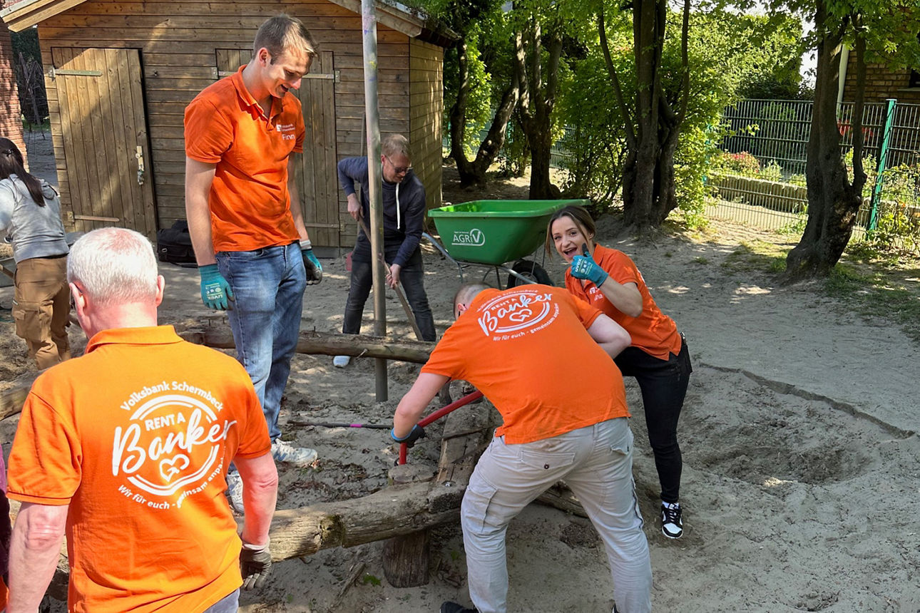 Fünf Personen stehen an und um einen alten Holzrahmen in einem großen Sandkasten.