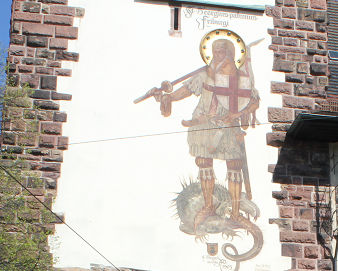Gemälde eines Heiligen mit Schwert und Drachen an einer Steinmauer mit weißem Putzfeld.