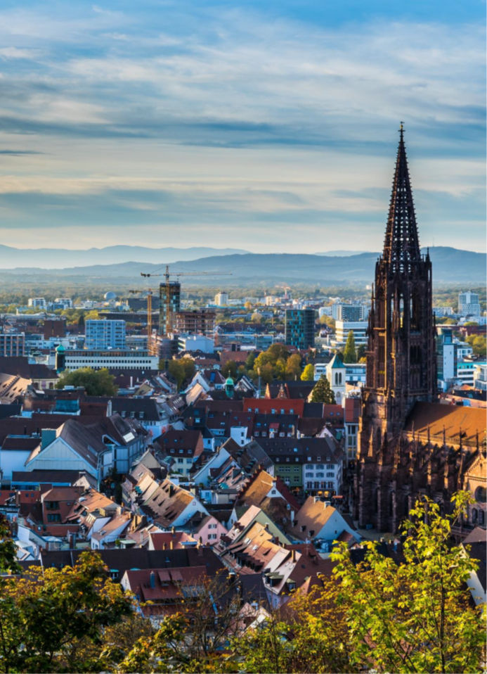 Stadtpanorama mit markantem Kirchturm, Wohngebäuden und Berglandschaft im Hintergrund.