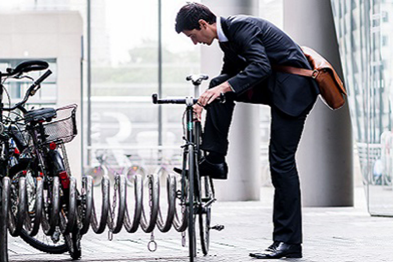 Businessman parking his bicycle in town at a bicycle rack after commuting to work in a concept of eco-friendly transport and healthy active lifestyle, panoramic banner view