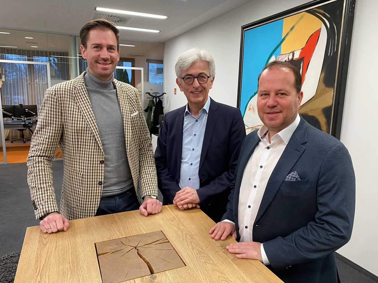 3 Männer vor einer bunten Wand an einem Stehtisch