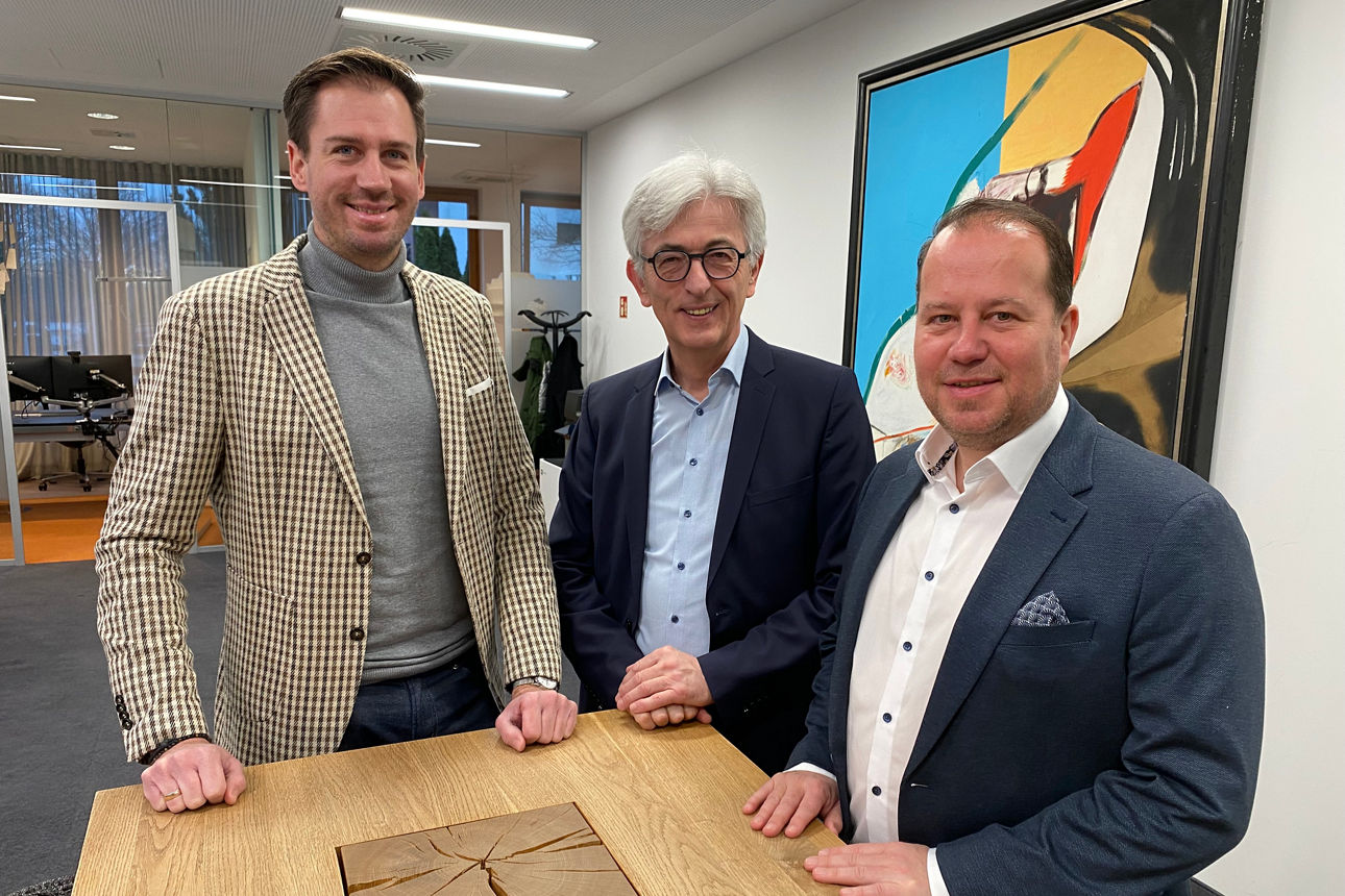 3 Männer vor einer bunten Wand an einem Stehtisch