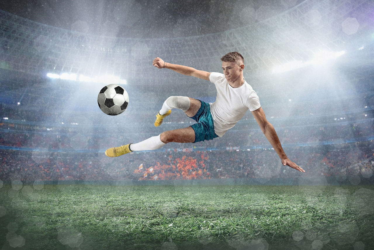 EinFußballer macht im Stadion bei Flulicht einen Seitfallzieher