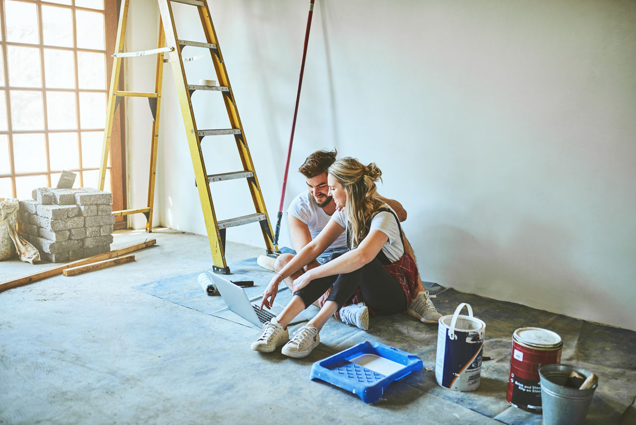 Junges Pärchen sitzt mit Notebook auf der Baustelle