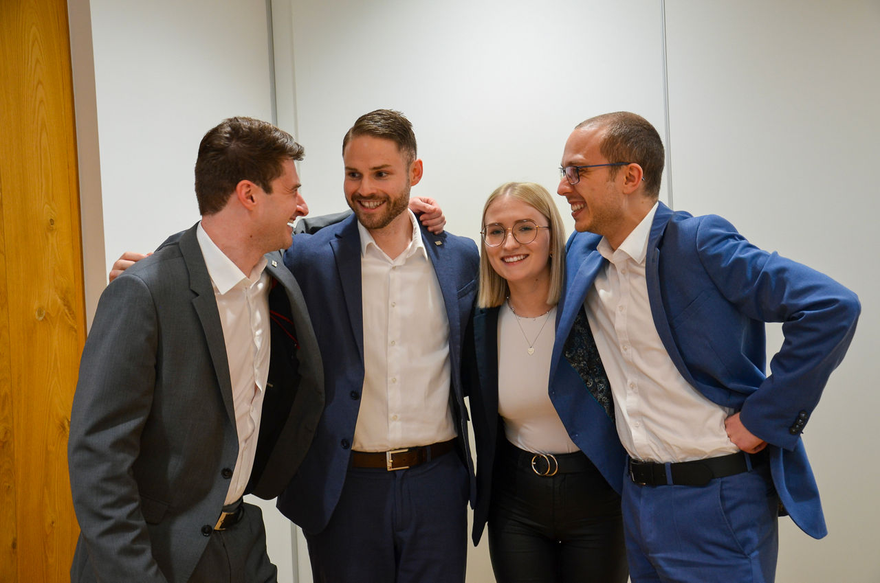 Vier freundliche junge Menschen, die sich in den Armen halten und lachen.