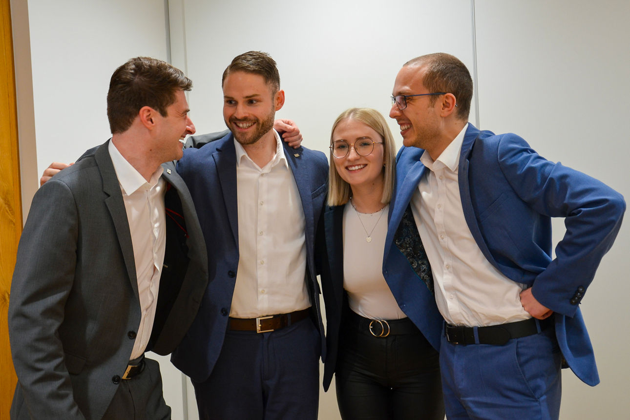 Vier freundliche junge Menschen, die sich in den Armen halten und lachen.