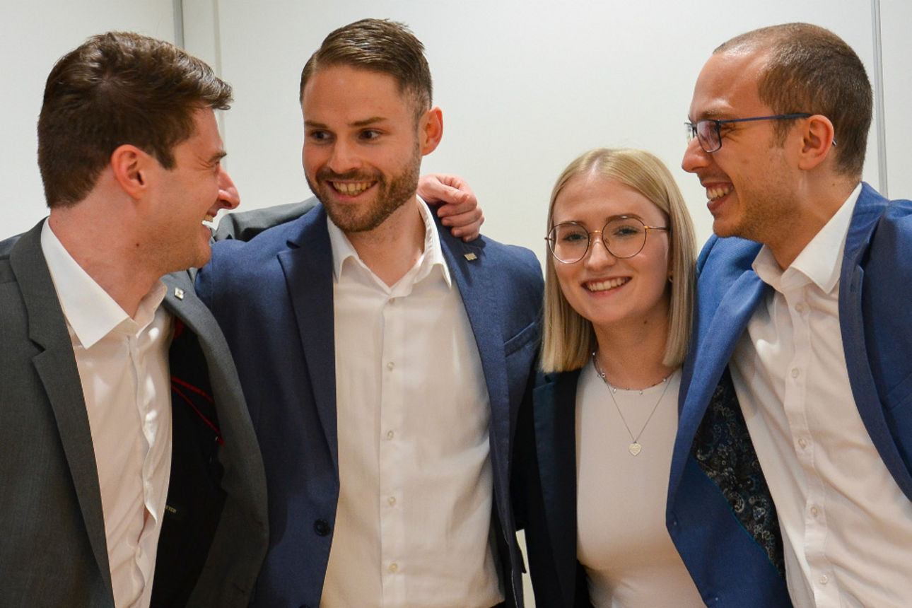 Vier freundliche junge Menschen, die sich in den Armen halten und lachen.