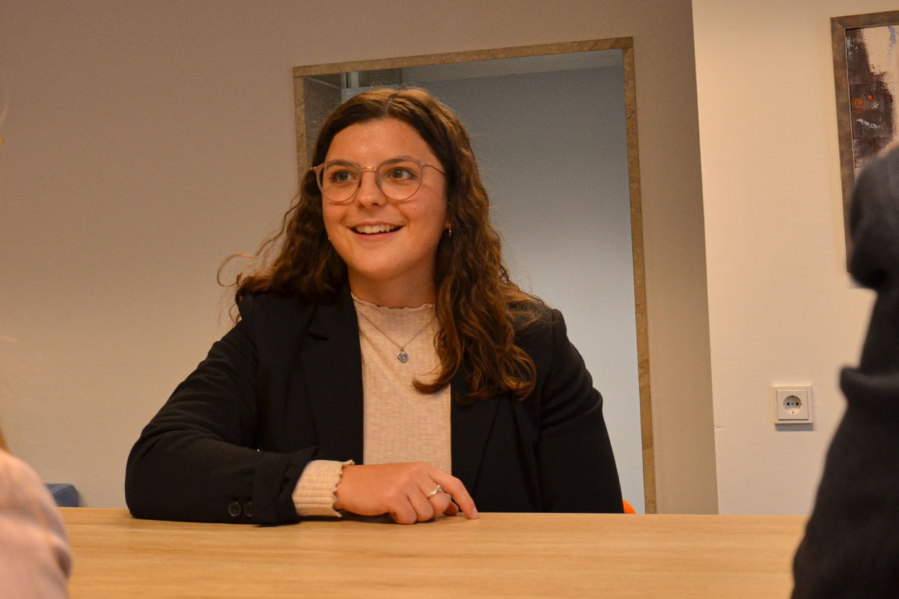 Eine junge Dame sitzt lachend an einem Tisch mit zwei weiteren jungen Personen.