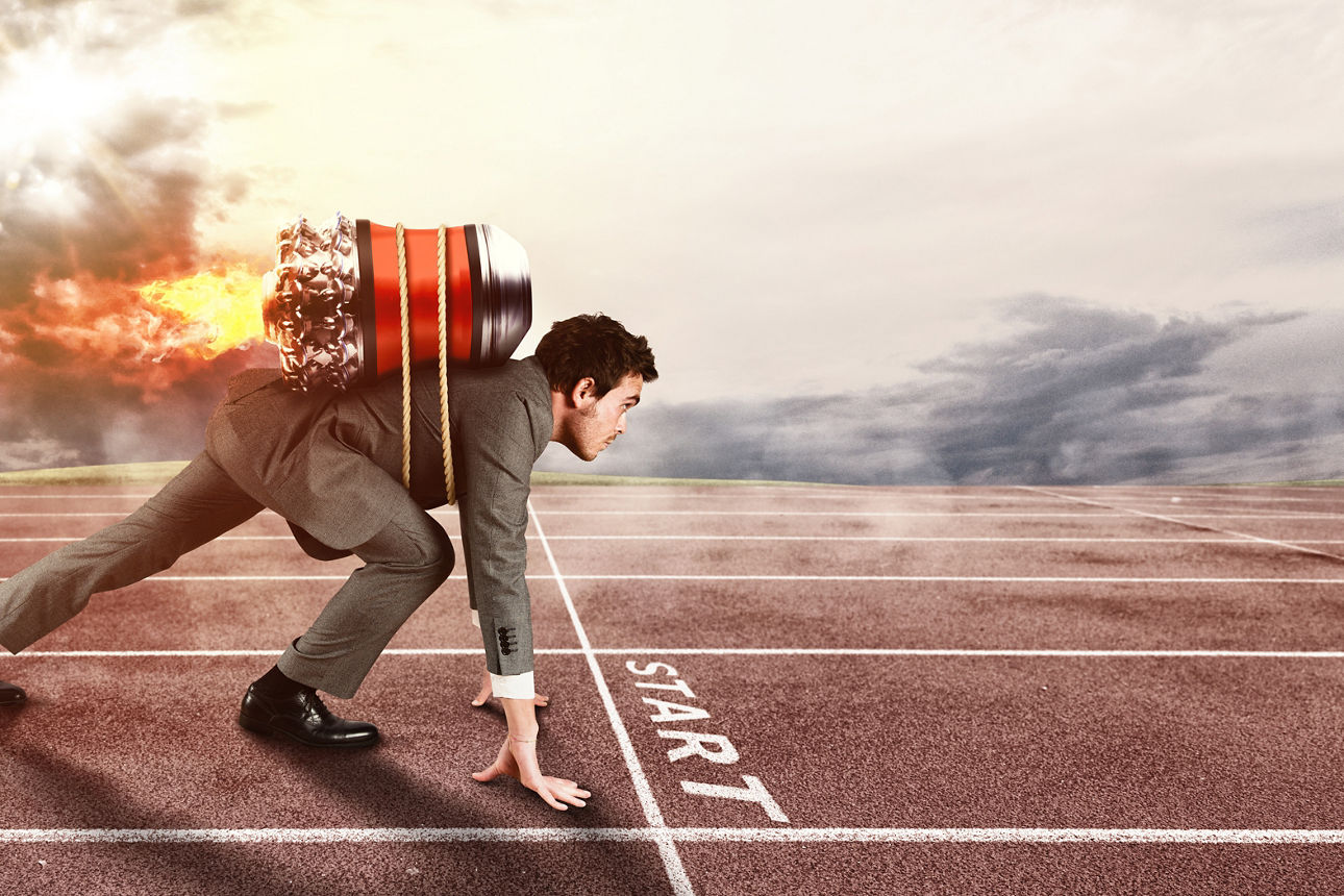 Ein Mann im Anzug in Startposition auf einer Laufbahn mit einem brennenden Raketenrucksack auf dem Rücken, vor der Startlinie