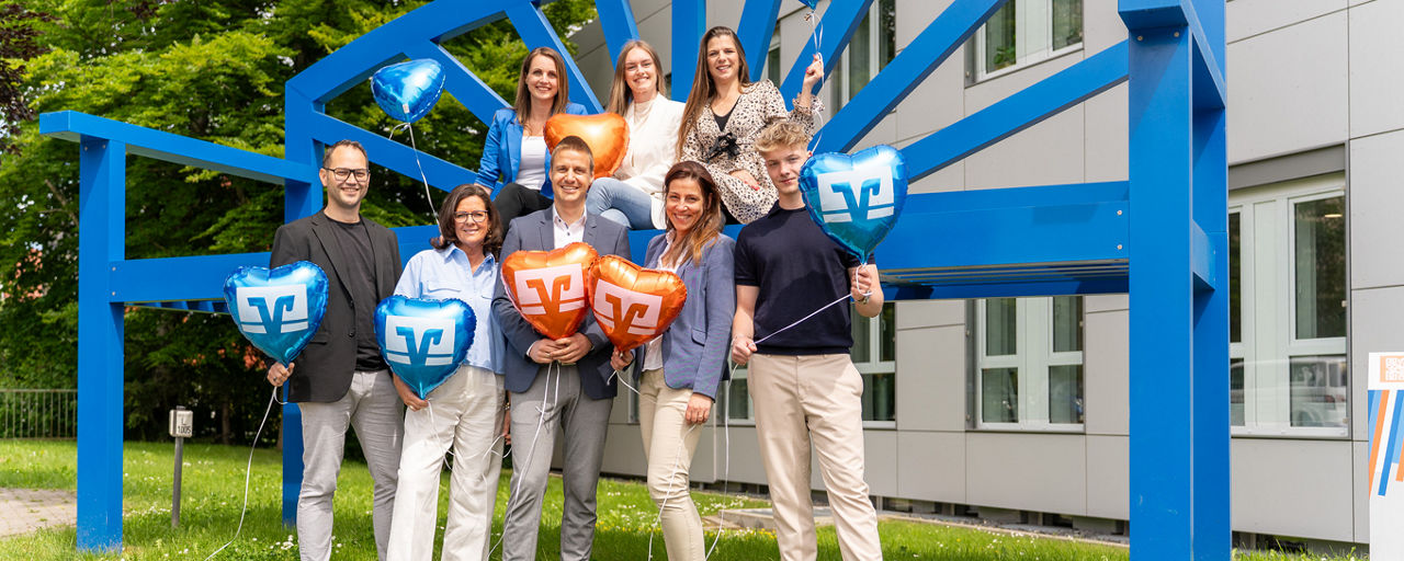 Personengruppe vor einer blauen Bank mir Luftballons in der Hand