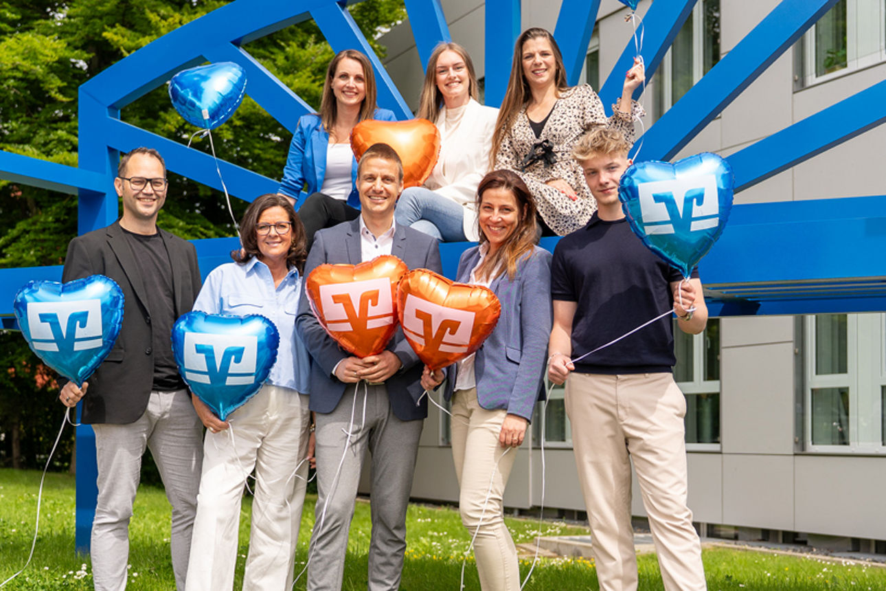 Personengruppe vor einer blauen Bank mir Luftballons in der Hand