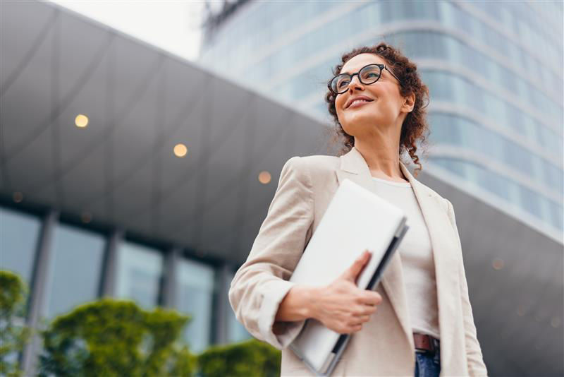 Business Frau mit einem Laptop in der Hand vor einem großen Gebäude.