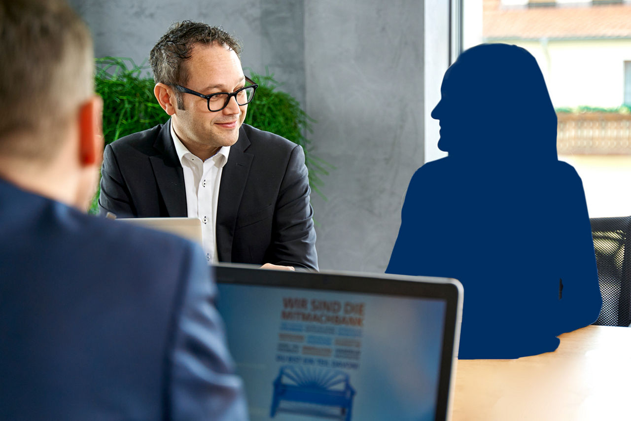 Ein Mann sitzt am Laptop und Ihm gegenüber ein Mann der auf eine Schattenfigur schaut