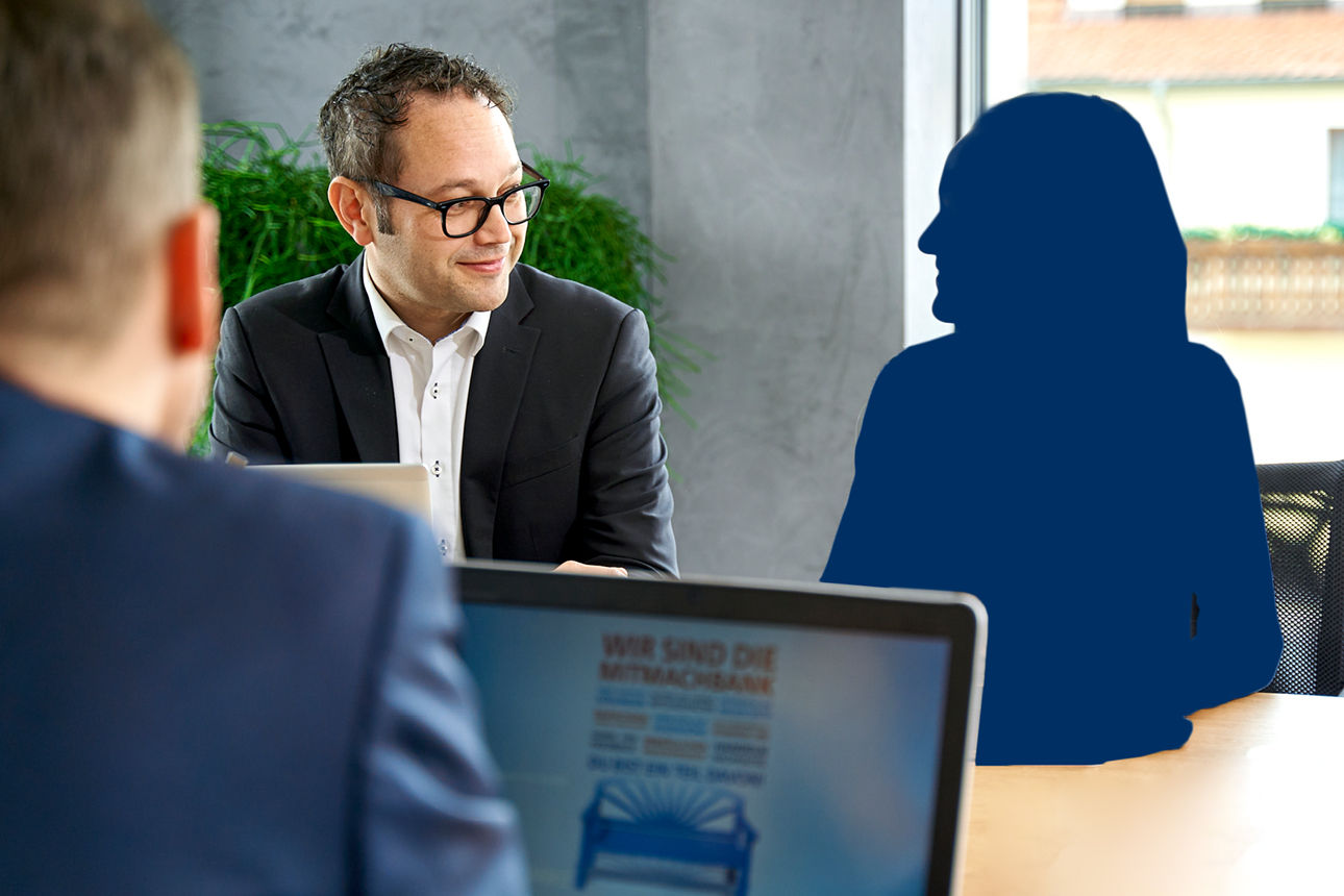 Ein Mann sitzt am Laptop und Ihm gegenüber ein Mann der auf eine Schattenfigur schaut