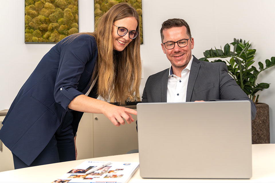 Frau und Mann am Schreibtisch schauen gemeinsam auf einen Laptop