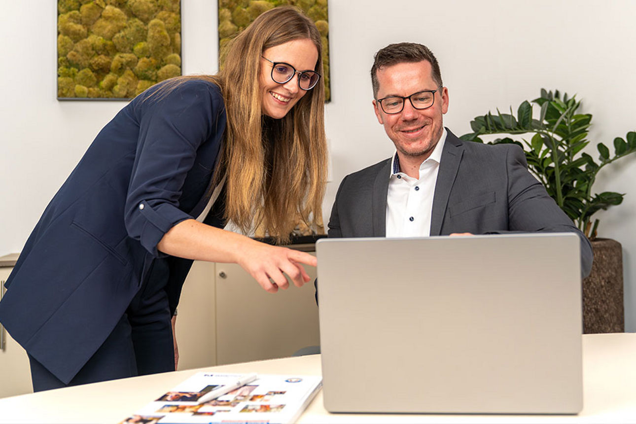 Frau und Mann am Schreibtisch schauen gemeinsam auf einen Laptop