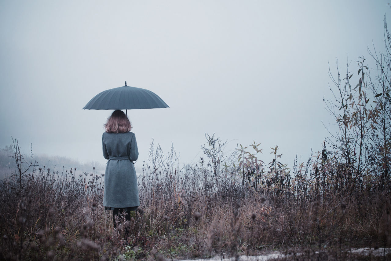 Frau mit einem Regenschirm steht in einem Feld