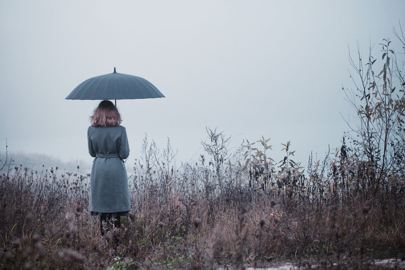 Frau mit einem Regenschirm steht in einem Feld