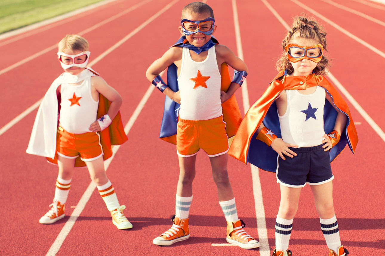 Drei Kinder in Superheldenkostümen stehen auf einer Laufstrecke