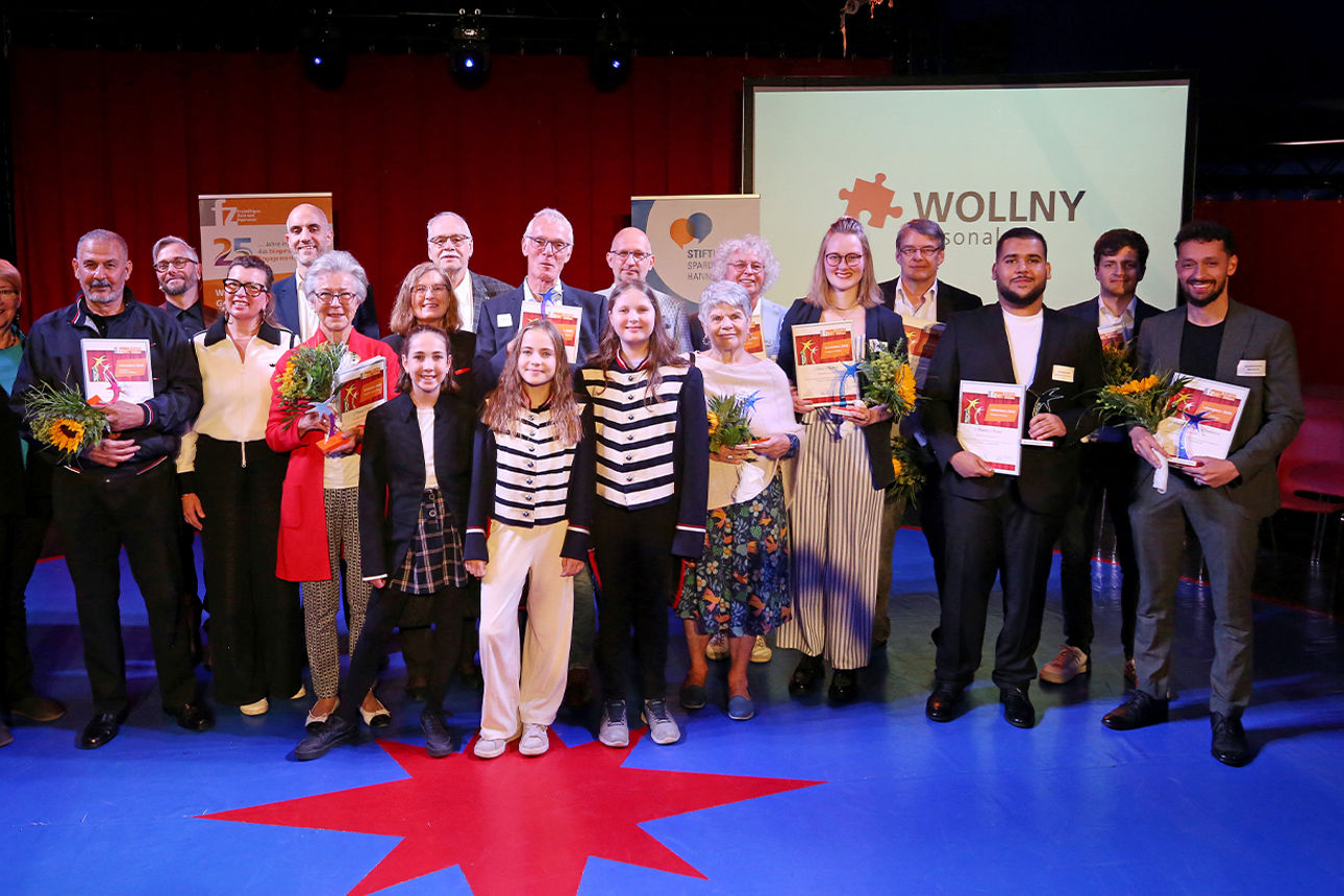 Ein große Gruppe Menschen steht auf einer Bühne und hat Urkunden in den Händen