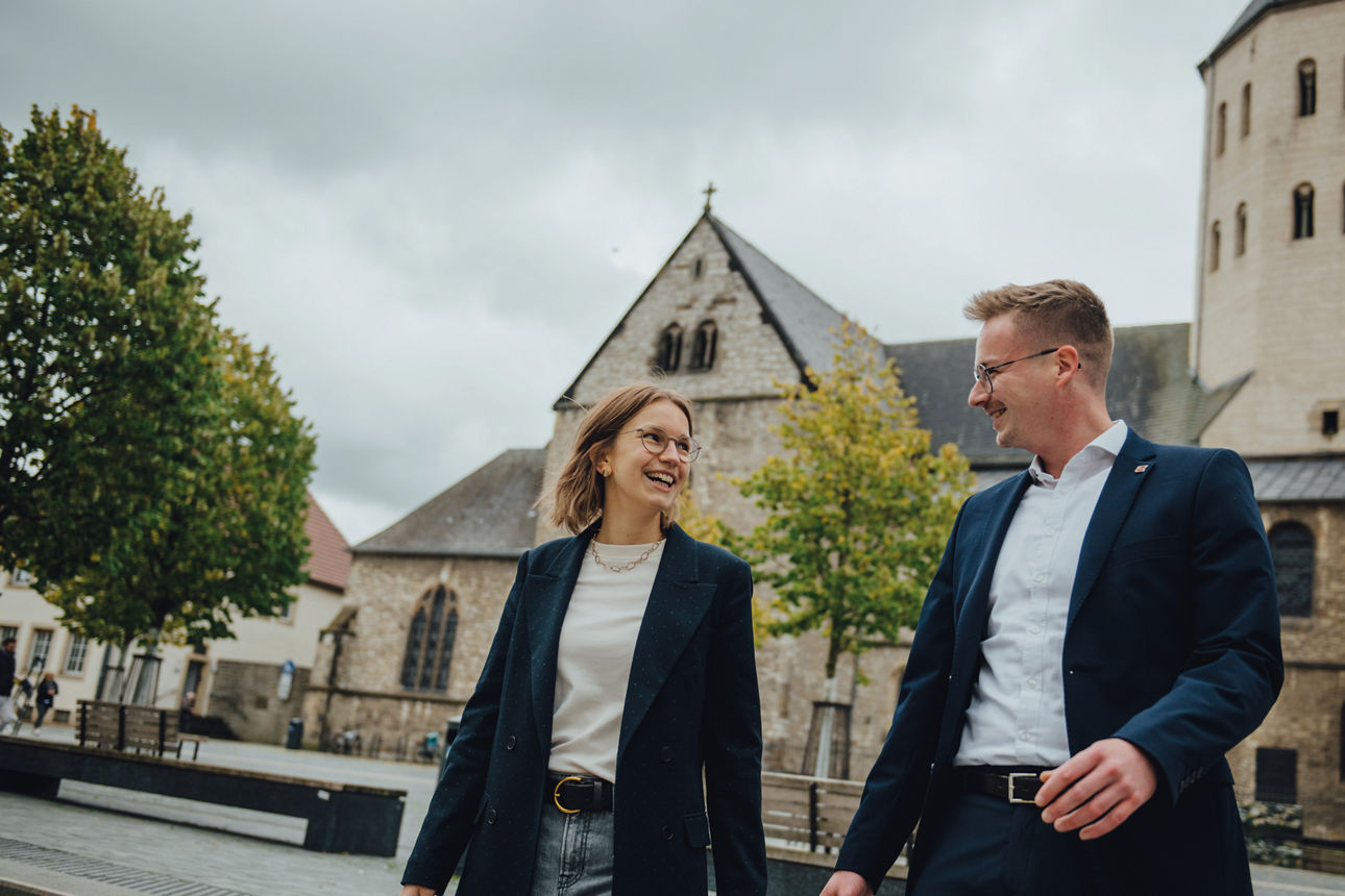 Zwei Mitarbeitende stehen vor einer Kirche und unterhalten sich