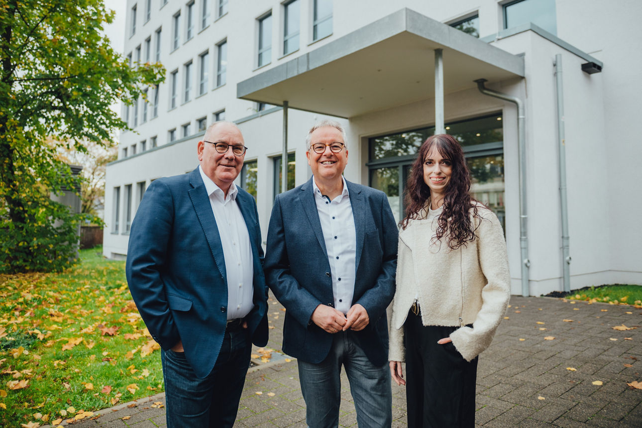 Drei Mitarbeitende stehen vor einem Gebäude