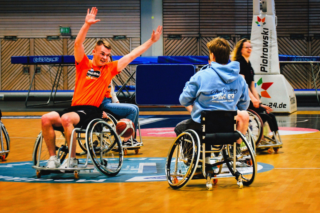 Zwei junge Männer sitzen im Rollstuhl und spielen Basketball