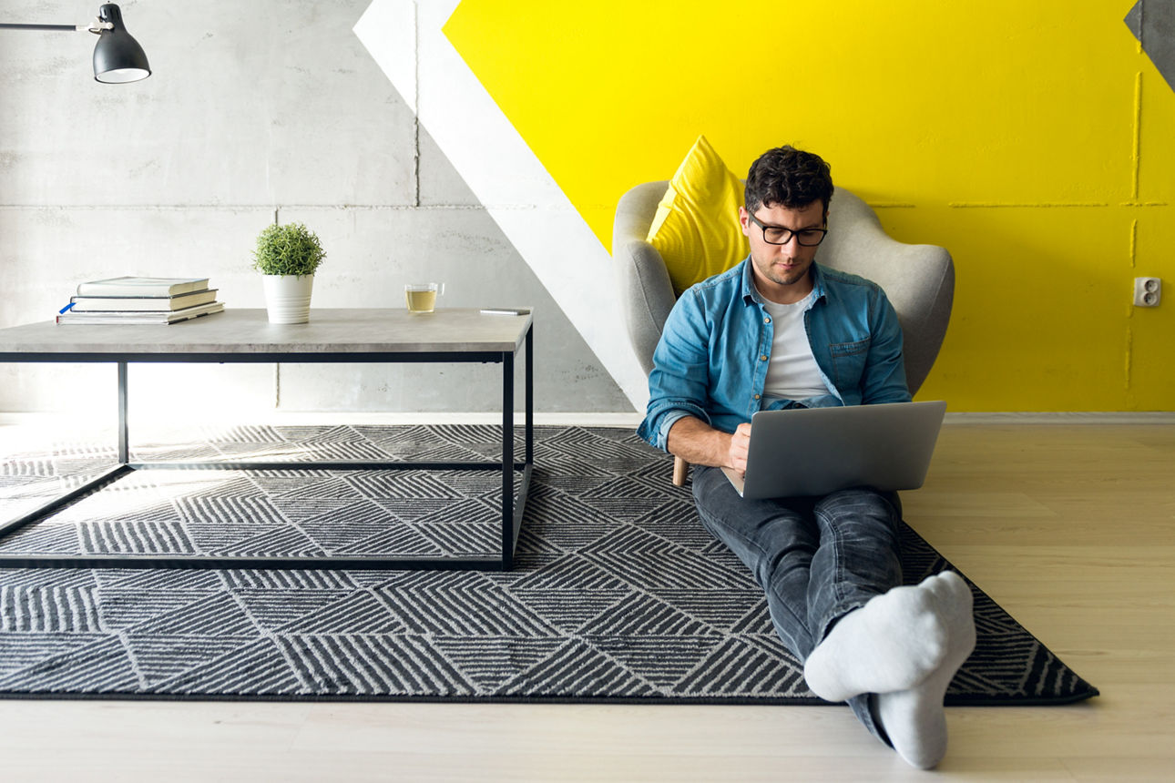 Lässig gekleideter Typ, der in einem einfachen und modernen Raum arbeitet. Die dominante Farbe des Raumes ist Gelb.