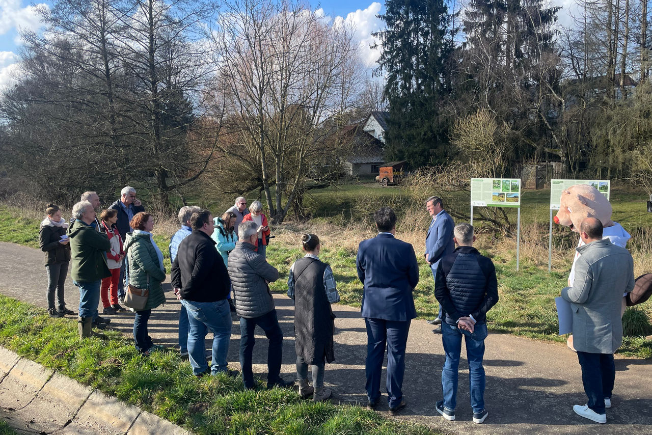 Große Gruppe Menschen steht vor Wiese mit Informationstafel
