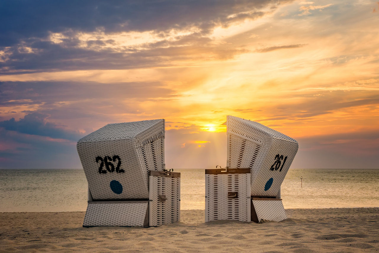 Zwei leere Strandkörbe am Meer bei Sonnenuntergang, mit den Nummern 261 und 262.
