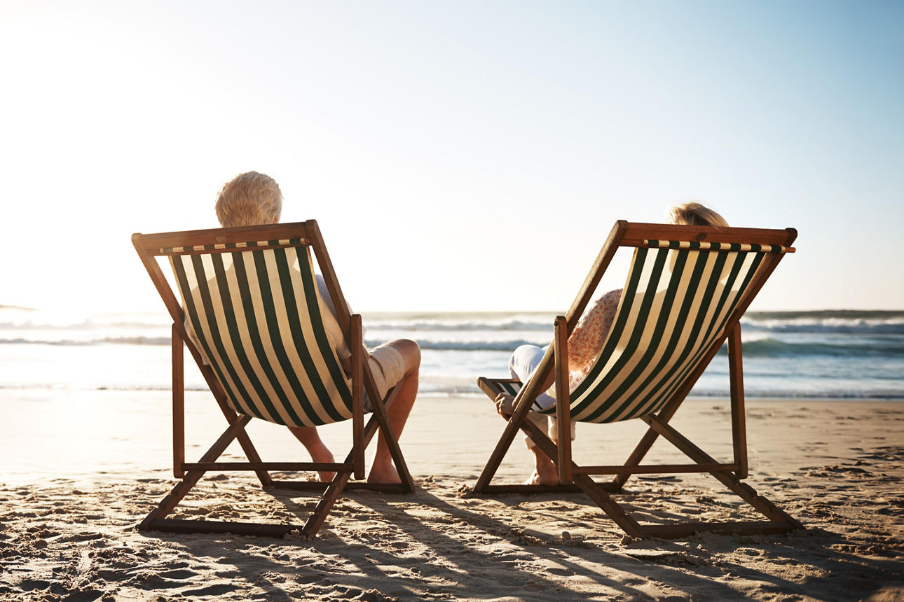 Rearview shot of a senior couple relaxing in beach chairs while looking at the view over the water