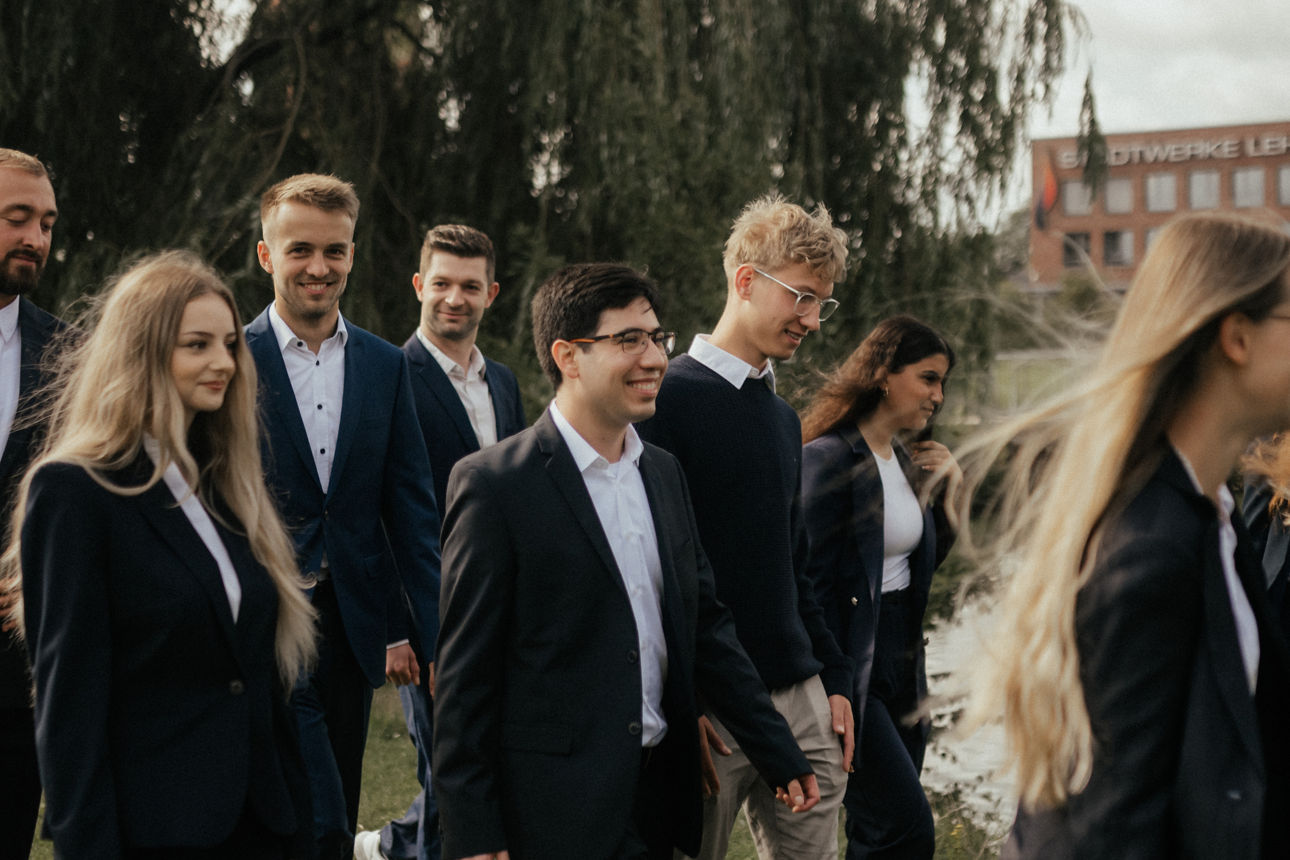 Eine Gruppe junger Erwachsener läuft draußen vor einer Trauerweide entlang.