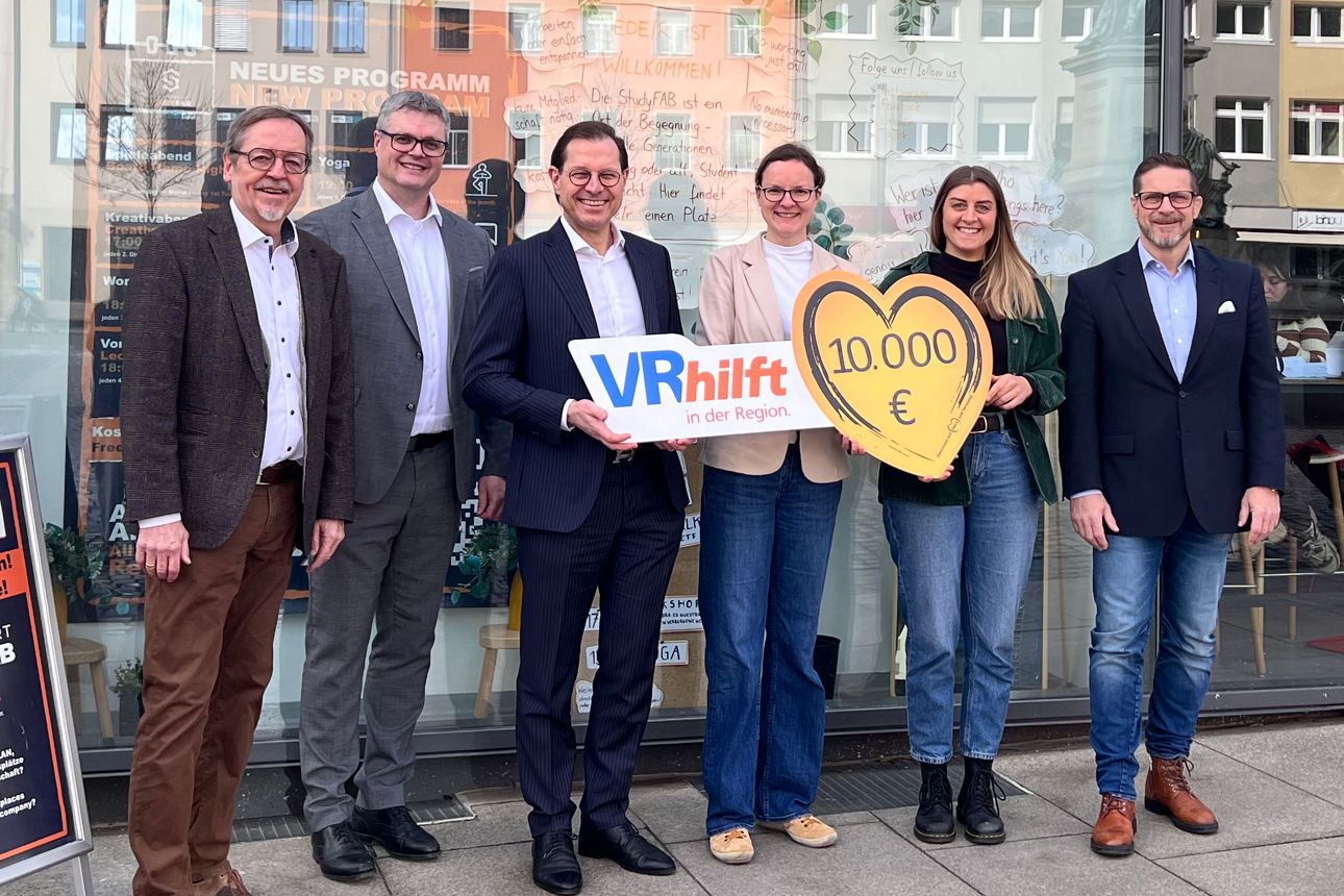 Der Vorsitzende und stellvertretende Vorsitzende der VR-Bank Schweinfurt-Stiftung übergeben einen Spendenscheck in Herzform mit der Spendensumme von 10.000 Euro an die Verantwortlichen des Vereins netSWerk.  Die sechs Personen stehen vor dem Gebäude der StudyFab in Schweinfurt.